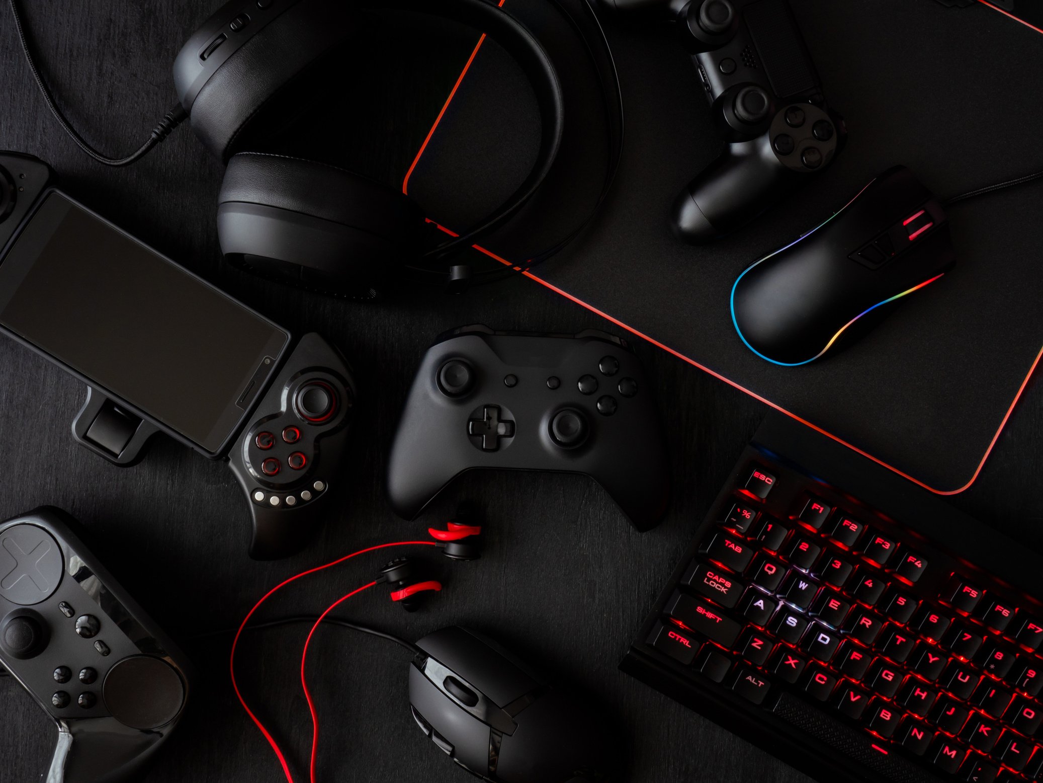 gamer workspace concept, top view a gaming gear, mouse, keyboard, joystick, headset, mobile joystick, in ear headphone and mouse pad on black table background.